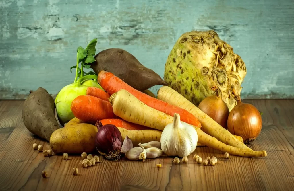 A variety of vegetables, including carrots and root vegetables, arranged on a wooden table, showcasing natural foods in a still life composition. - Exercise Is Keeping People Fat But No One Wants to Talk About It